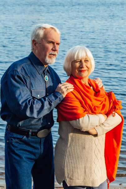 cheerful senior citizens woman and man are standing and hugging on the lake, against the background of the bridge. - Valokuva, kuva