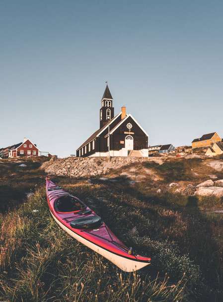 Canoe in front of old wodden Zions Church in arctic city of Ilulissat, with midnight sun light and blue sky in North Greenland - Foto, imagen