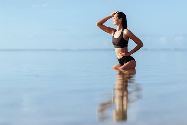 Outdoor shot of smiling young female model in bikini standing against blue sky. - Foto, Imagen
