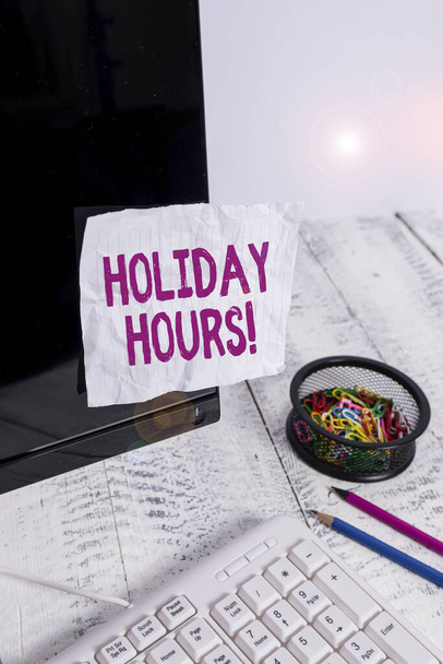 Text sign showing Holiday Hours. Conceptual photo Overtime work on for employees under flexible work schedules Note paper taped to black computer screen near keyboard and stationary. - Photo, Image