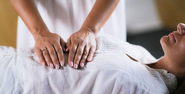 Naisterapeutti Reiki-hoidon suorittaminen. Kädet naisen vatsan yläpuolelle. Vaihtoehtoisen hoidon käsite, stressin vähentäminen ja rentoutuminen
.   - Valokuva, kuva