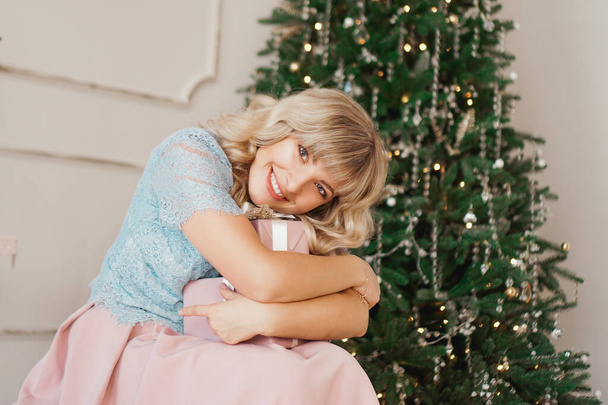 Mujer joven encantadora con estilo elegante sentado en el interior con regalo de Navidad rosa
 - Foto, imagen