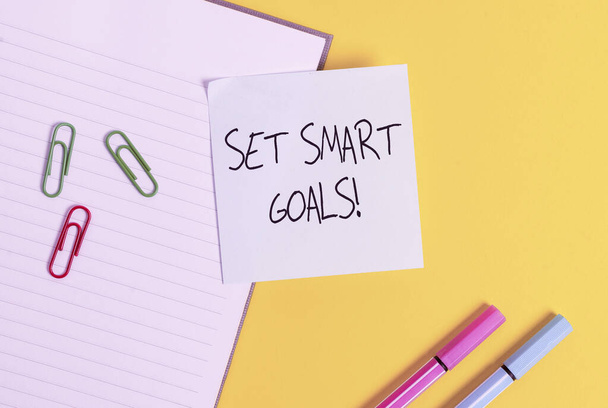 Word writing text Set Smart Goals. Business concept for list to clarify your ideas focus efforts use time wisely Empty blue paper with copy space paper clips and pencils on the yellow table. - 写真・画像