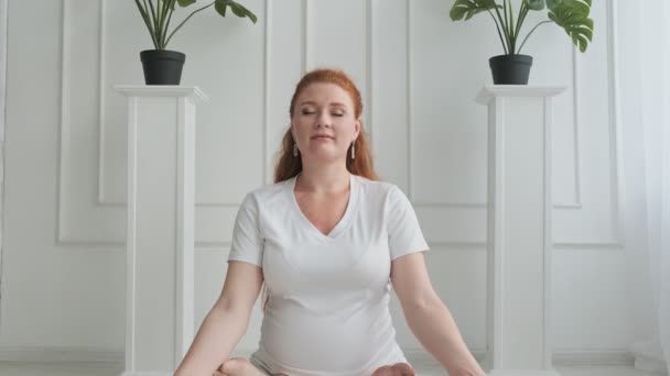 Young pregnant woman practicing yoga. Female sitting in lotus position. - Materiaali, video