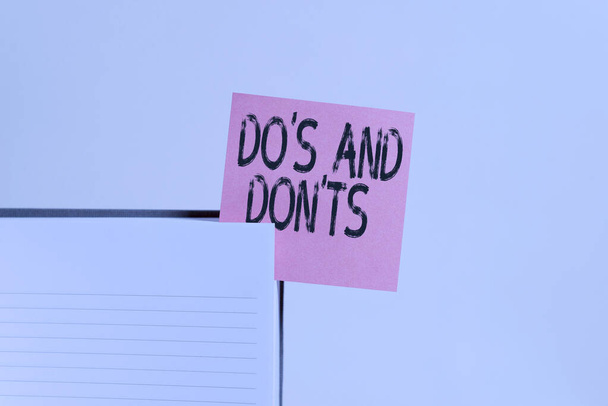 Text sign showing Do S And Don tS. Conceptual photo Rules or customs concerning some activity or actions Upper view lined hard cover note book sticky note inserted clear background. - 写真・画像
