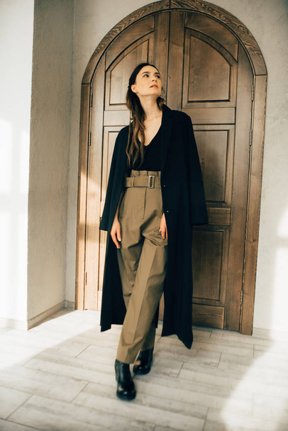 houkutteleva brunette nainen muoti tyyli vaatteita poseeraa lähellä puinen ovi
  - Valokuva, kuva
