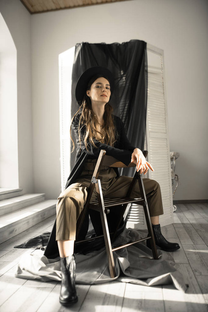 houkutteleva brunette nainen muoti tyyli vaatteita istuu tuolilla ja poseeraa studiossa
  - Valokuva, kuva