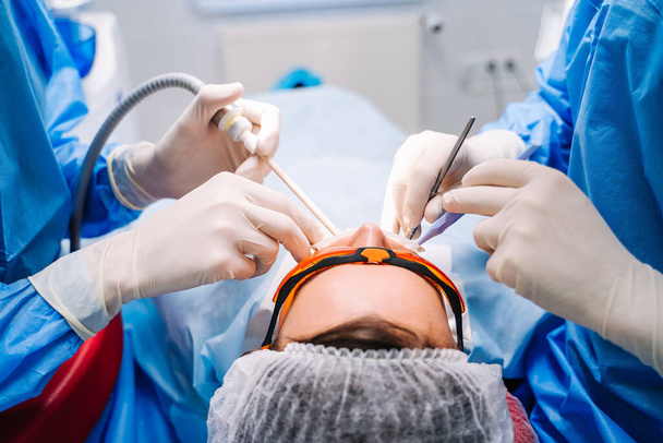 Dentist in uniform perform dental treatment on a patient at modern stomatology office. Selective focus. View from the back. Closeup. - 写真・画像