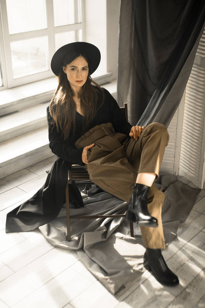 jolie femme brune dans des vêtements de style mode assis sur une chaise et posant en studio
  - Photo, image