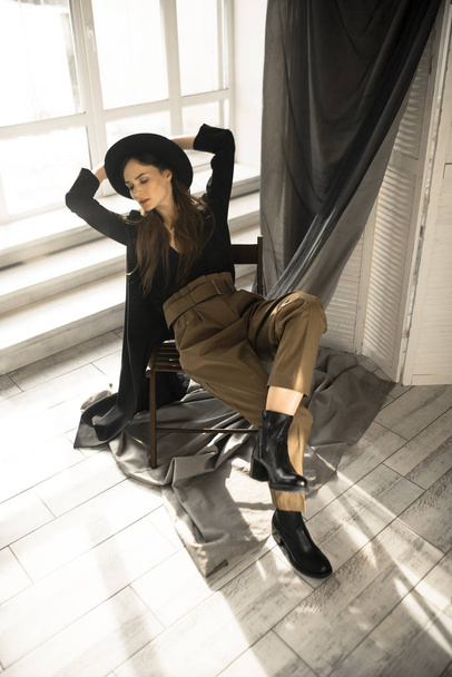 attraente donna bruna in stile moda vestiti seduti sulla sedia e in posa in studio
  - Foto, immagini