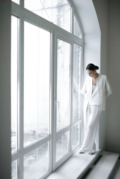 fashion style woman in white clothes posing near window in studio  - 写真・画像