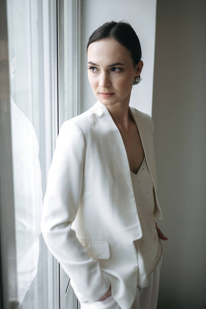 módní styl žena v bílém oblečení pózování v blízkosti okna ve studiu  - Fotografie, Obrázek