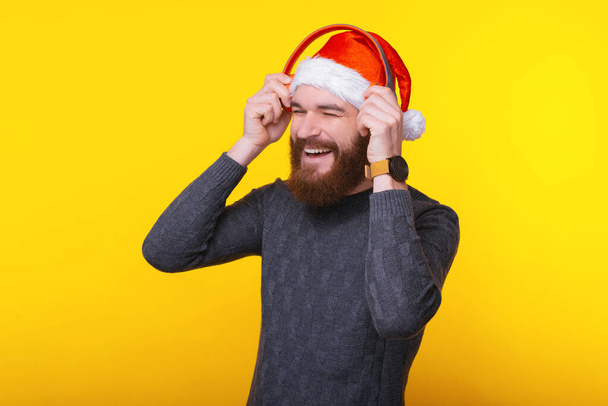 Onnellinen mies yllään joulupukin hattu ja kuunnella musiikkia punainen kuulokkeet
 - Valokuva, kuva
