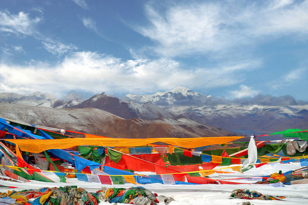 Tibeti imádkozó zászlók előtt a Yamdrok-tó, tükrözve a barna színek a Mt. Naiqinkangsang a kék tiszta égbolton. - Fotó, kép