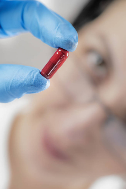 Γυναίκα επιστήμονας κρατώντας κόκκινο χάπι με μπλε γάντια στο εργαστήριο. Νέο χάπι έννοια της έρευνας - Φωτογραφία, εικόνα