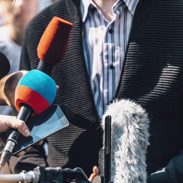 Δημοσιογράφοι παίρνουν συνέντευξη από άνδρα ομιλητή και κρατούν μικρόφωνα και κινητά τηλέφωνα.  - Φωτογραφία, εικόνα