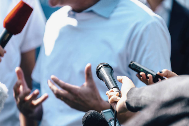 Δημοσιογράφοι παίρνουν συνέντευξη από άνδρα ομιλητή και κρατούν μικρόφωνα και κινητά τηλέφωνα. - Φωτογραφία, εικόνα