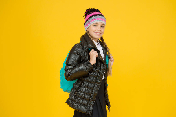Schoolgirl fashion outfit. Fall autumn winter. Child with backpack. Fashion shop. Girl wear knitted hat and jacket yellow background. Fashion concept. Warm clothing. Buy clothes for school season - Valokuva, kuva