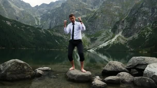 Επιτυχημένος επιχειρηματίας χαρούμενος από τη νίκη, τρελά χαρούμενα συναισθήματα και χορός κοντά σε μια λίμνη στα βουνά το ηλιοβασίλεμα - Πλάνα, βίντεο