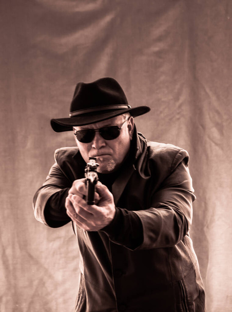 Egy fekete ruhás férfi, fekete bőrkabátban, kalapban. Ganster szivarral és fegyverekkel, egy Mauser rendszer pisztollyal. Mafiosi fekete szemüvegben, sötét háttérrel. veszélyes, barátságtalan, gonosz, goromba ember. Cowboy bűnöző.  - Fotó, kép