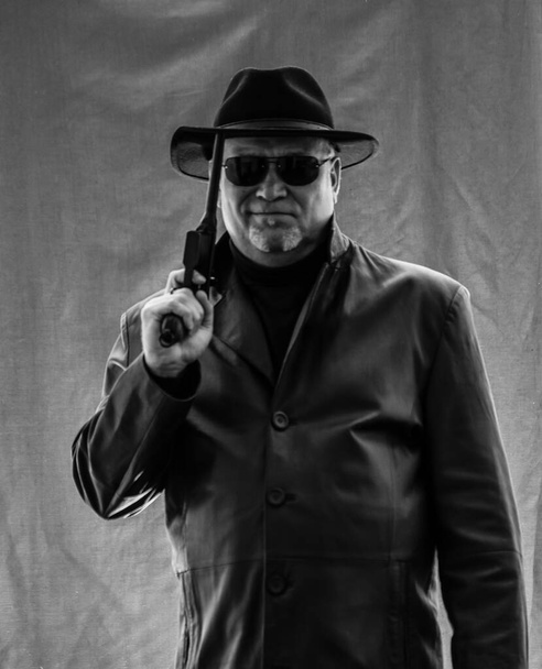 Mies mustissa vaatteissa, musta nahkatakki, hattu. Ganster sikarin ja aseita, Mauser järjestelmän pistooli. Mafioso mustissa laseissa tummalla pohjalla. vaarallinen, epäystävällinen, paha, töykeä mies. Cowboy-rikollinen
  - Valokuva, kuva
