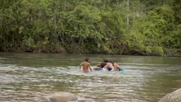 Rdzenni chłopcy grają w rzece z pływającą oponą - Materiał filmowy, wideo