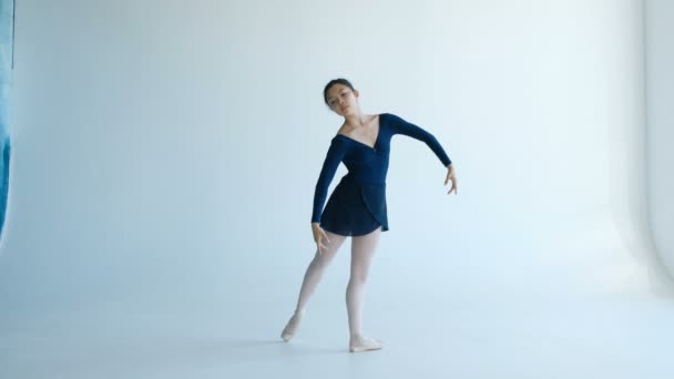 Aantrekkelijke ballerina voert professionele danselementen uit op een witte achtergrond - Video