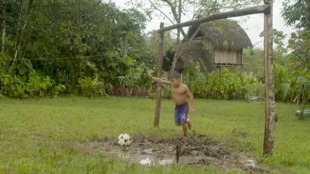 Malý domorodý chlapec hraje fotbal venku ve své venkovské vesnici - Záběry, video