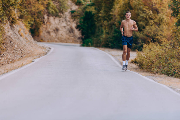 Man shirtloze joger rennend in de bergen onder zonlicht - Foto, afbeelding