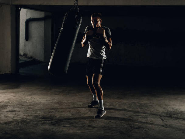 Silhouette muscular fighter training on a punching bag in the gy - 写真・画像