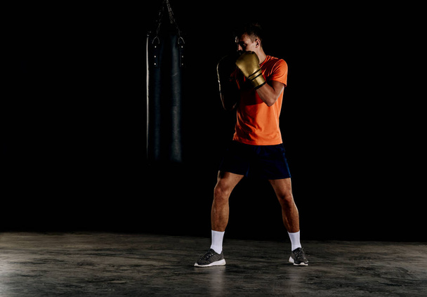 Fit professional boxing man kicking at punching bag - Photo, Image