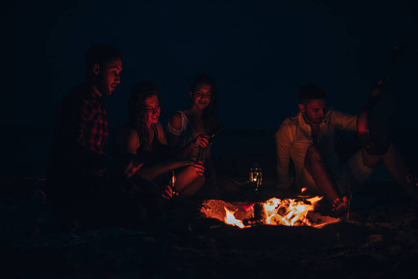 Vrienden genieten van muziek in de buurt van kampvuur bij nacht - Foto, afbeelding