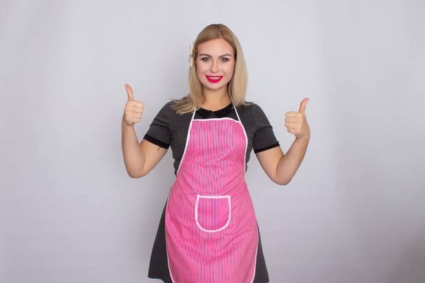 Blonde woman in grey dress wearing kitchen white and ppink apron - Foto, imagen