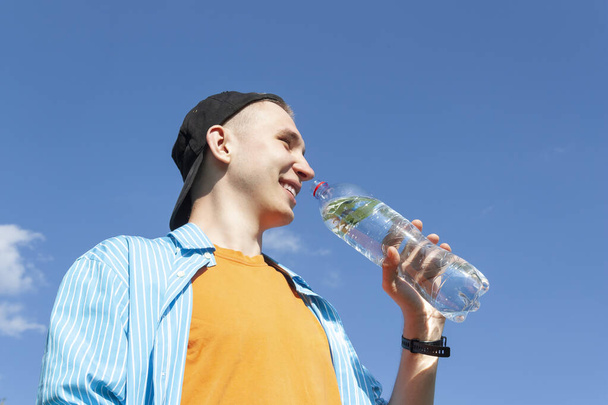 Facet pijący wodę z butelki przeciwko błękitnemu niebu - Zdjęcie, obraz