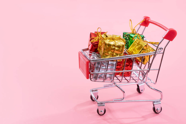 Annual sale, Christmas shopping season concept - mini red shop cart trolley full of gift box isolated on pale pink background, copy space, close up - Photo, image