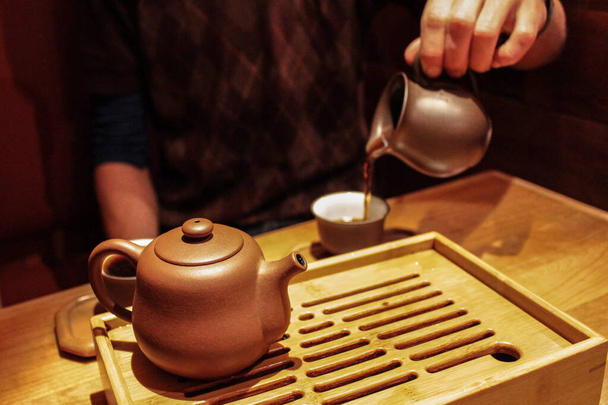 dunkler Pu-Erh-Tee aus einem lila Tongefäß in eine kleine Verkostungstasse gießen - Foto, Bild