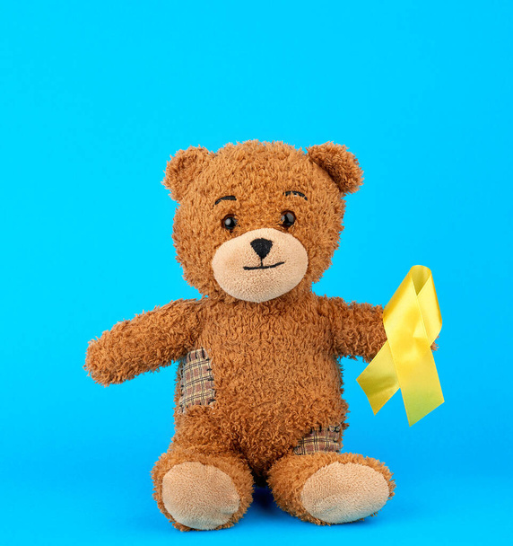bruine teddybeer zit en houdt in zijn poot een geel zijden lint  - Foto, afbeelding