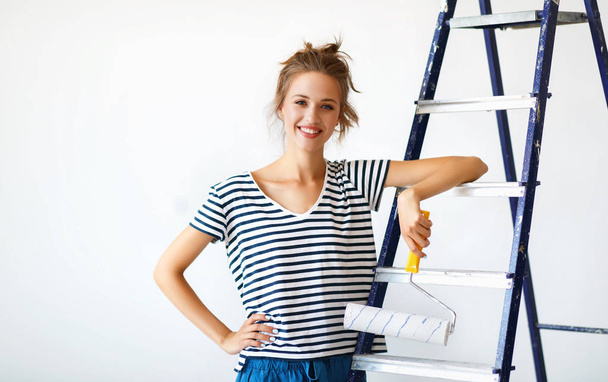 Repair in apartment. Happy young woman paints wall - Фото, изображение