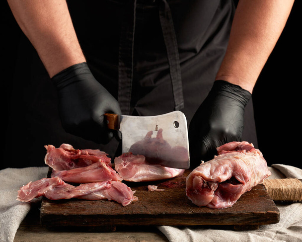 σεφ με μαύρα γάντια λατέξ κρατά ένα μεγάλο μαχαίρι και κόβει σε κομμάτια - Φωτογραφία, εικόνα
