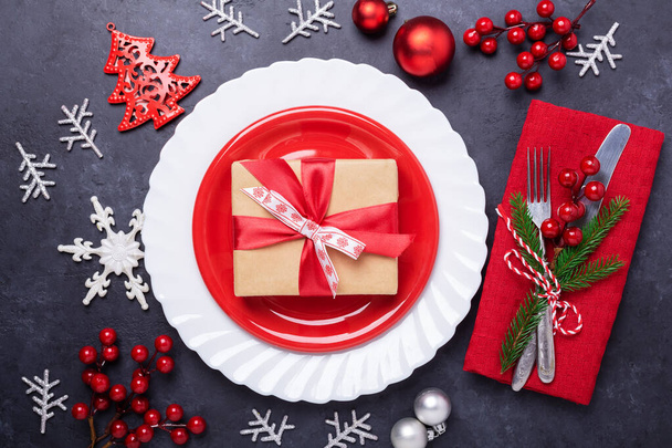 Christmas table place setting with red plate, gift box, cutlery with festive decorations star bow on stone background - Zdjęcie, obraz