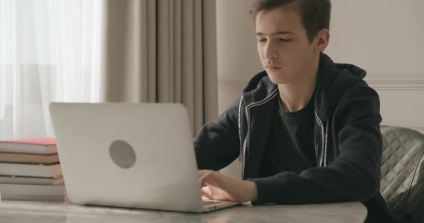 Teen boy doing school lessons at home. Student writes the homework. Child learns. Boy using laptop. Student writes with a pen in a notebook. - Záběry, video