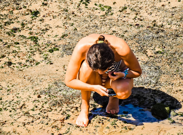 Женщина в полосатом купальнике фотографирует с мобильного телефона
 - Фото, изображение