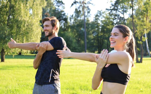Young couple stretching muscles outdoors in park at sunny day. - Fotoğraf, Görsel