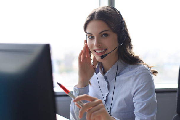 Beautiful smiling call center worker in headphones is working at modern office - Fotó, kép