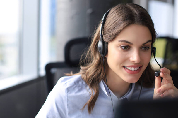 Beautiful smiling call center worker in headphones is working at modern office - Foto, afbeelding