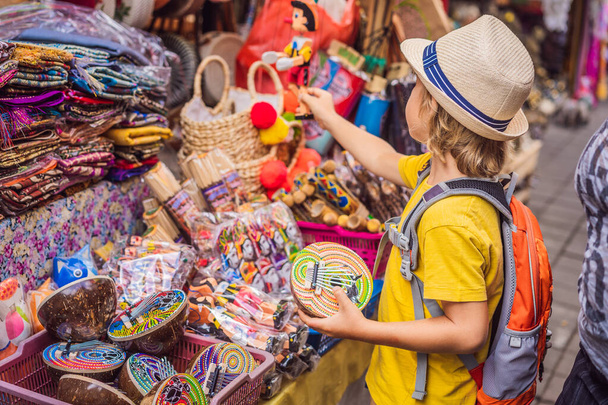 Boy at a market in Ubud, Bali. Typical souvenir shop selling souvenirs and handicrafts of Bali at the famous Ubud Market, Indonesia. Balinese market. Souvenirs of wood and crafts of local residents - 写真・画像