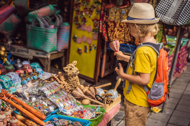 Boy at a market in Ubud, Bali. Typical souvenir shop selling souvenirs and handicrafts of Bali at the famous Ubud Market, Indonesia. Balinese market. Souvenirs of wood and crafts of local residents - Foto, imagen