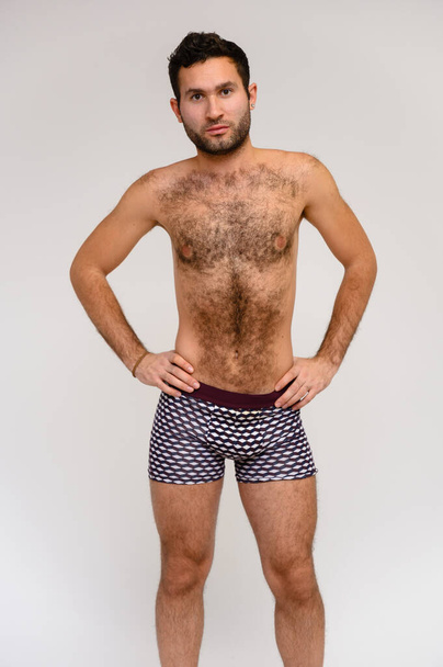 Portrait of a handsome male model with perfect body, standing naked in shorts, posing on a white background. Black hair. Close Studio Shot - Foto, Imagen