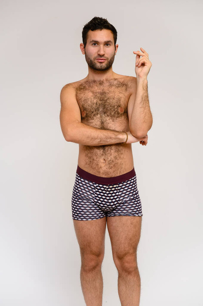 Portrait of a handsome male model with perfect body, standing naked in shorts, posing on a white background. Black hair. Close Studio Shot - Foto, Imagem