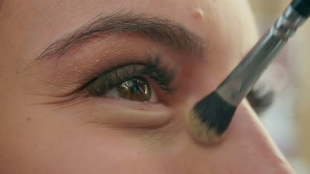 Μακιγιάζ για όμορφη νεαρή κοπέλα στο σαλόνι ομορφιάς εφαρμόζοντας σκιά ματιών - Πλάνα, βίντεο